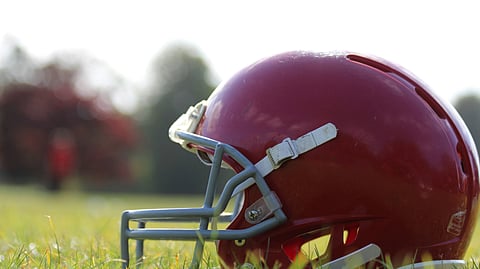 A red football helmet resting on green grass under natural lighting.