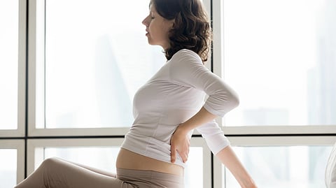  A pregnant woman sitting on a bed, appears to be experiencing back pain.