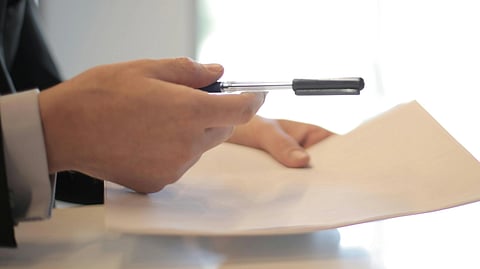 Image of a person giving pen to another person to sign a document.