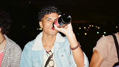 Image of three young men sitting on a bench, enjoying beers.