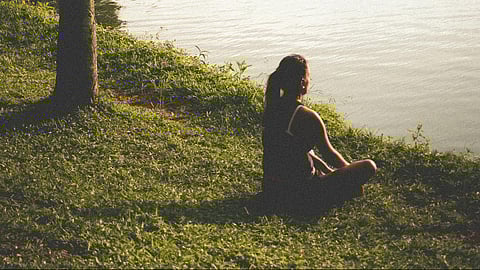 An image of a woman sitting near lake on grass.