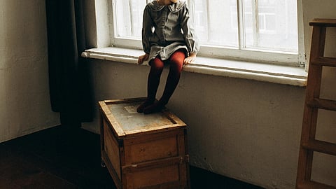 Image of a girl child sitting besides a window.