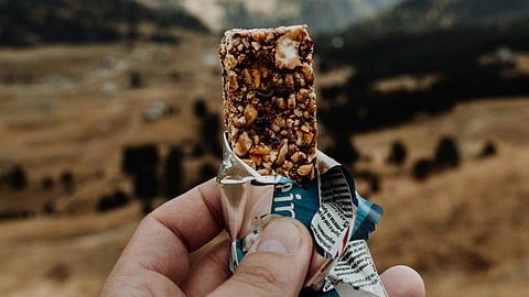 A person holds a bar of chocolate with scenic mountains in the background.
