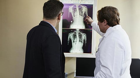 Two men examine an X-ray in a room, discussing its details and implications for a medical diagnosis.