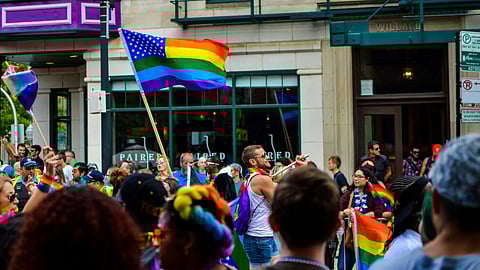 A diverse group of people stands in a street, proudly holding rainbow flags to celebrate LGBTQ+ pride and unity.