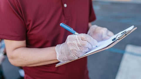 A man in a red shirt is writing on a clipboard, focused on his task in a well-lit environment.