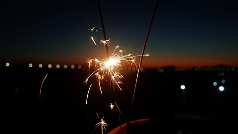 Image of a person holding a lit sparkler against a dark background.