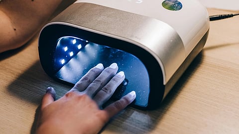 Image of a woman applies artificial nails using a nail machine in a well-lit salon setting.