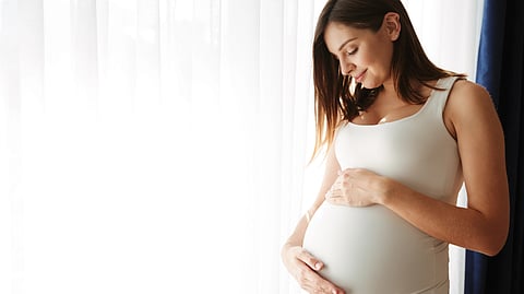 A pregnant woman wearing a white t-shirt is caressing her baby. 