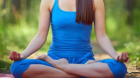 A woman in blue meditates peacefully among the trees in a serene forest setting.