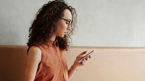 Image of a woman wearing brown shirt using her phone while sitting on a sofa.