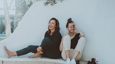 Two women sitting on a bench, sharing a joyful moment and laughing together.