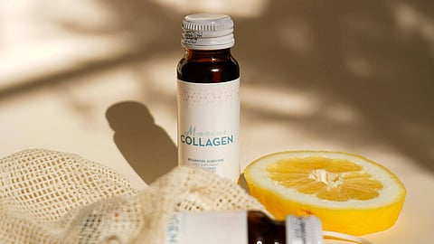 A bottle of collagen supplement with a slice of orange besides it.