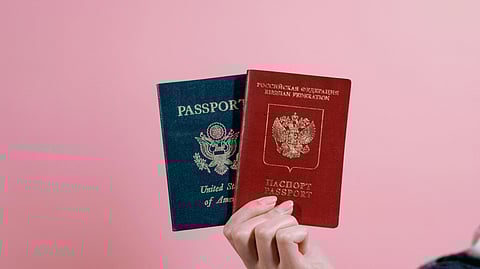 A person holds two passports against a pink background, symbolizing travel and dual citizenship.