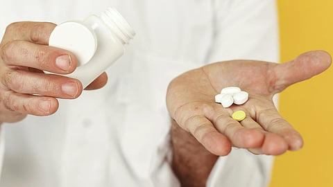 A man in a white lab coat holds pills in his hand.