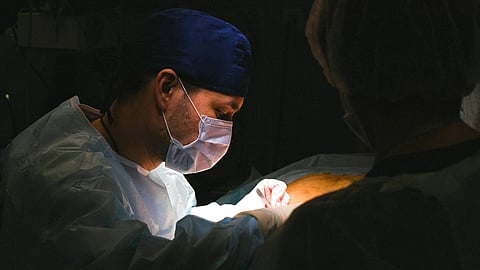 An image of a doctor performing surgery in a dim lit room.