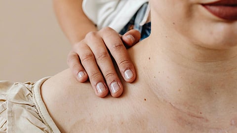 A woman wearing a head scarf on her shoulder, gazing thoughtfully off to the side.