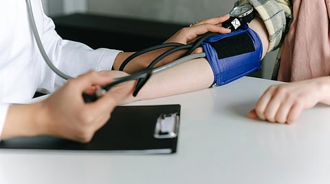 A doctor measures a patient's blood pressure using a sphygmomanometer in a clinical setting.