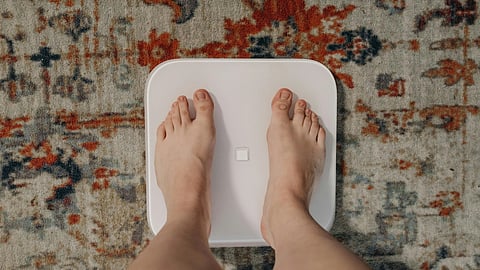 A person stands on a weight scale, looking down at the display, measuring their weight.