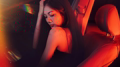 A woman sitting in a car illuminated by a red light, creating a dramatic atmosphere inside the vehicle.