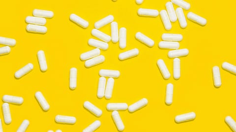 White pills scattered across a bright yellow background, creating a vibrant contrast.