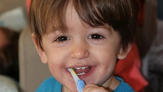 A boy in a blue t shirt holding a toothbrush in his mouth.