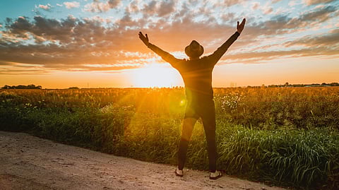 A man stands in a field at sunset, arms outstretched, embracing the warm glow of the evening sky.