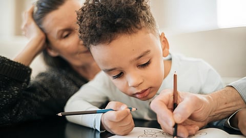 A child and his mother sit together, happily drawing on paper with colorful crayons.