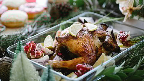Image of a whole chicken rests on a table surrounded by various dishes and food items.