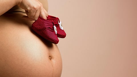 An image of a woman's pregnant belly and baby shoes kept on it.