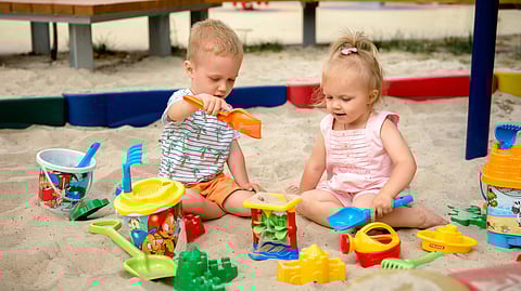 Image of two children happily playing in the sand, surrounded by colorful toys and building sandcastles.