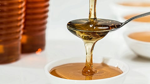A spoon is being filled with golden honey, glistening as it drips from the jar above.