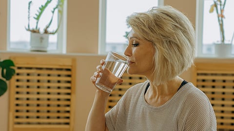 An elderly woman in black leggings sitting on yoga mat while drinking water