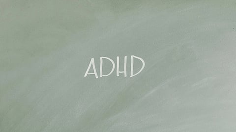 The word "ADHD" is written in white chalk on a dark green chalkboard.