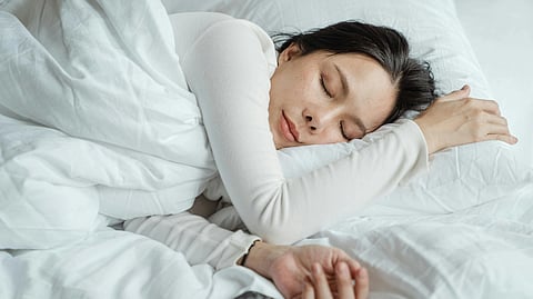 A woman sleeps peacefully on a white bed, head resting on her arm.