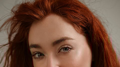 Portrait of a person with long, wavy red hair and a slight smile, against a neutral background. 