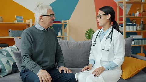A female medical professional conversing with an elderly male individual in his house