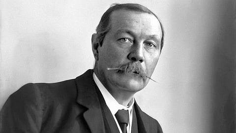 Conan Doyle in a three-piece suit with a thick mustache poses confidently against a textured chair.
