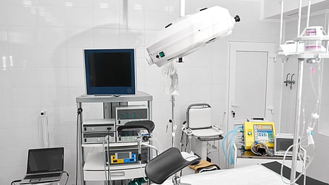 A sterile hospital room with medical equipment, including a monitor, defibrillator, and surgical table. 