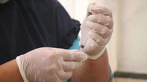 Close-up of gloved hands holding a syringe, preparing for injection.