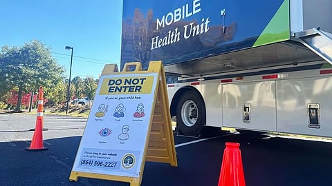 Mobile health unit with a "Do Not Enter" sign outside, listing symptoms like fever and cough.