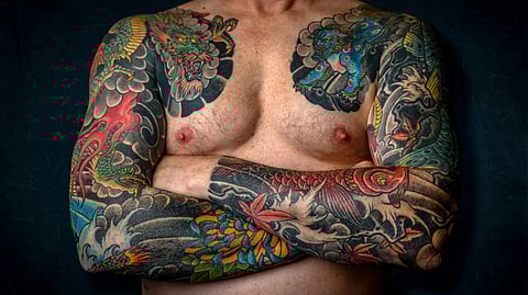 Shirtless man with vivid, intricate full-sleeve Japanese tattoos featuring dragons.
