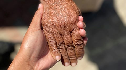 Image of an elderly woman gently holds the hand of a young person, symbolizing connection and support across generations.