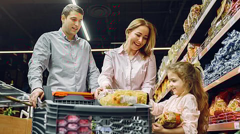 Image of a family of four shopping together in a supermarket aisle, examining products on the shelves.