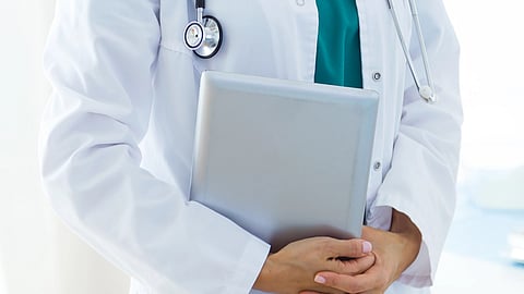 Image of a doctor wearing a white coat with a stethoscope and having a note pad in her hands.