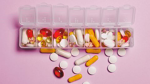 A plastic container filled with various pills, set against a soft pink background.