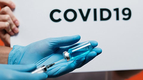 Image of a nurse drawing a COVID-19 vaccine from an ampoule, with a COVID-19 signboard in the background.