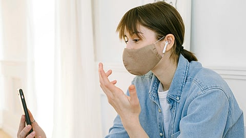 A woman wearing a face mask is using a cell phone.