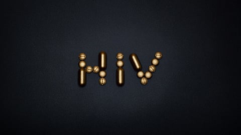 Image of the word "HIV" formed from gold pills arranged on a neutral background.