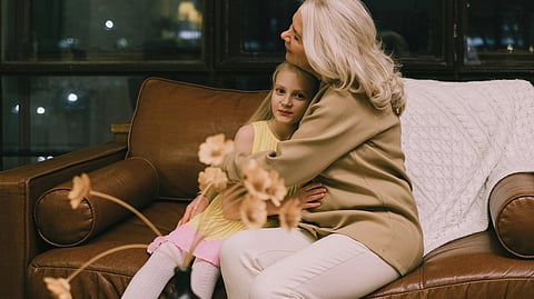 Image of a woman and a young girl sit together on a couch.